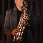 Primer plano del músico Jimmy Sax sonriendo mientras toca el saxofón en una presentación privada.
