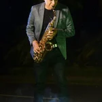 El saxofonista profesional Jimmy Sax tocando su instrumento con traje gris durante una sesión de portafolio.